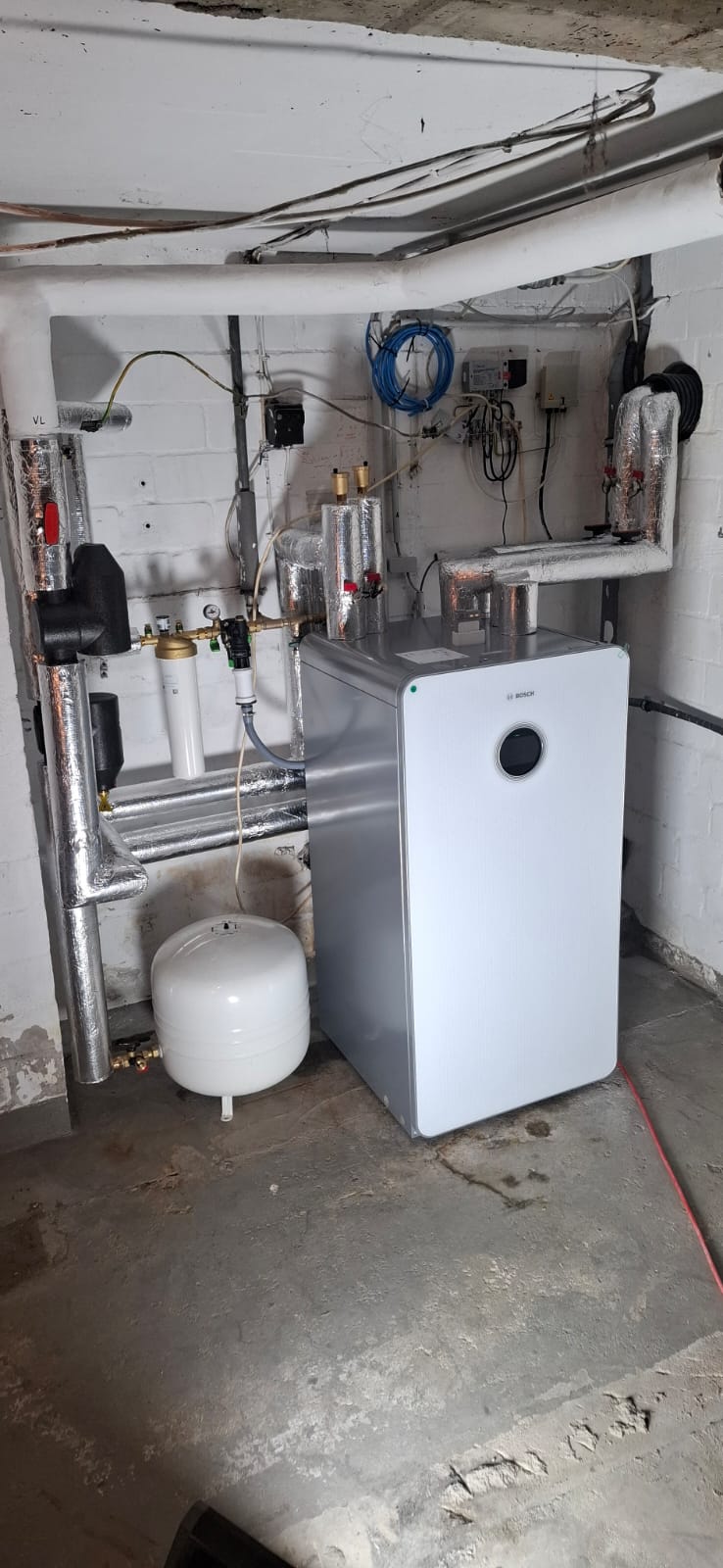 Innenaufgestellte Bosch-Wärmepumpe mit Speicher, Ausdehnungsgefäß und vollständig isolierter Rohrinstallation.